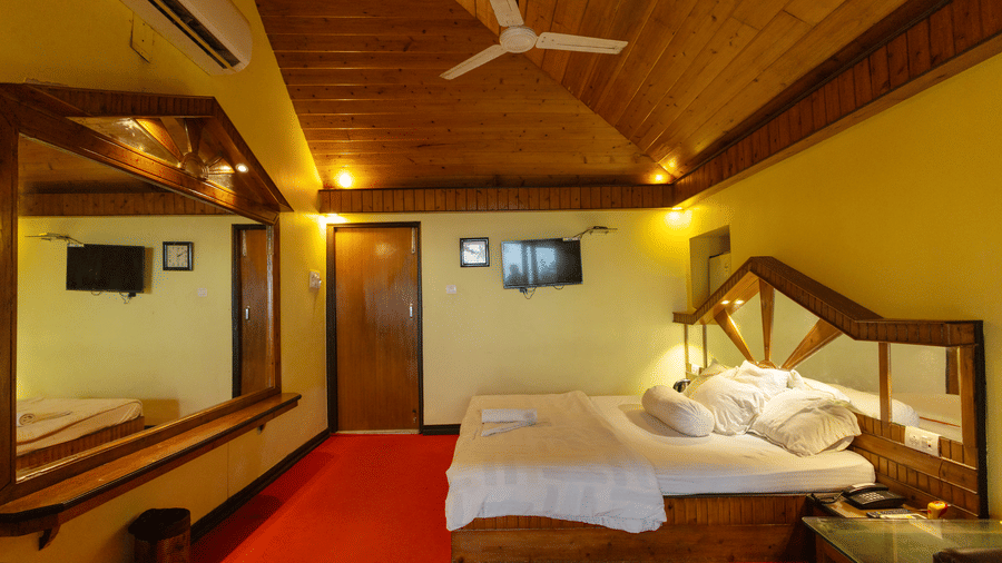A bedroom with a king size bed, a wooden ceiling, a large mirror, a bedside table, and a wall mounted TV at Hotel Seagull Digha.